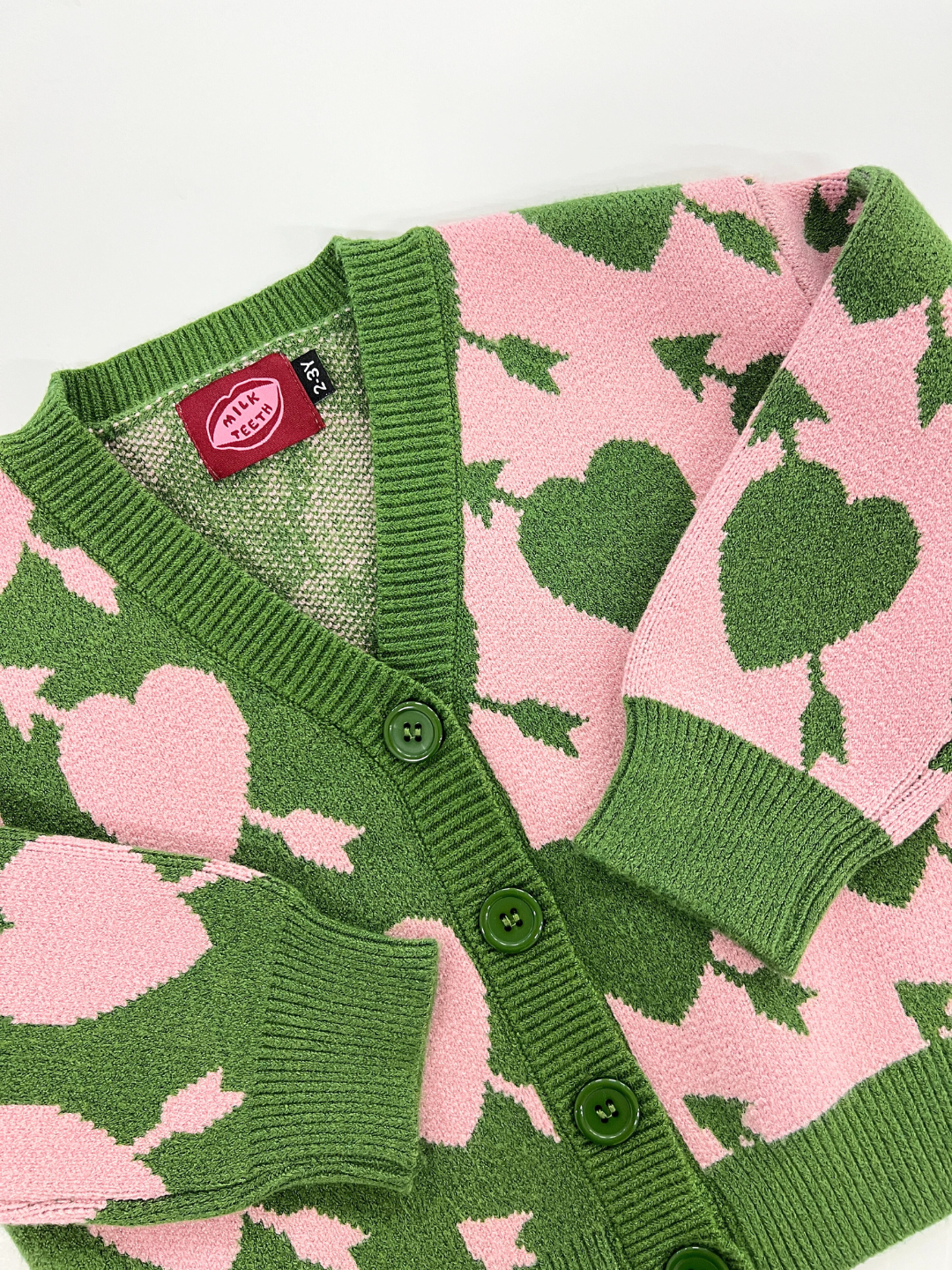 The LOVESTRUCK CARDIGAN is a green and pink sweater adorned with a pattern of large hearts and leaves. It includes an interior label bearing the name "Silly Silas." For more information, including measurements, please refer to the full description and photos.