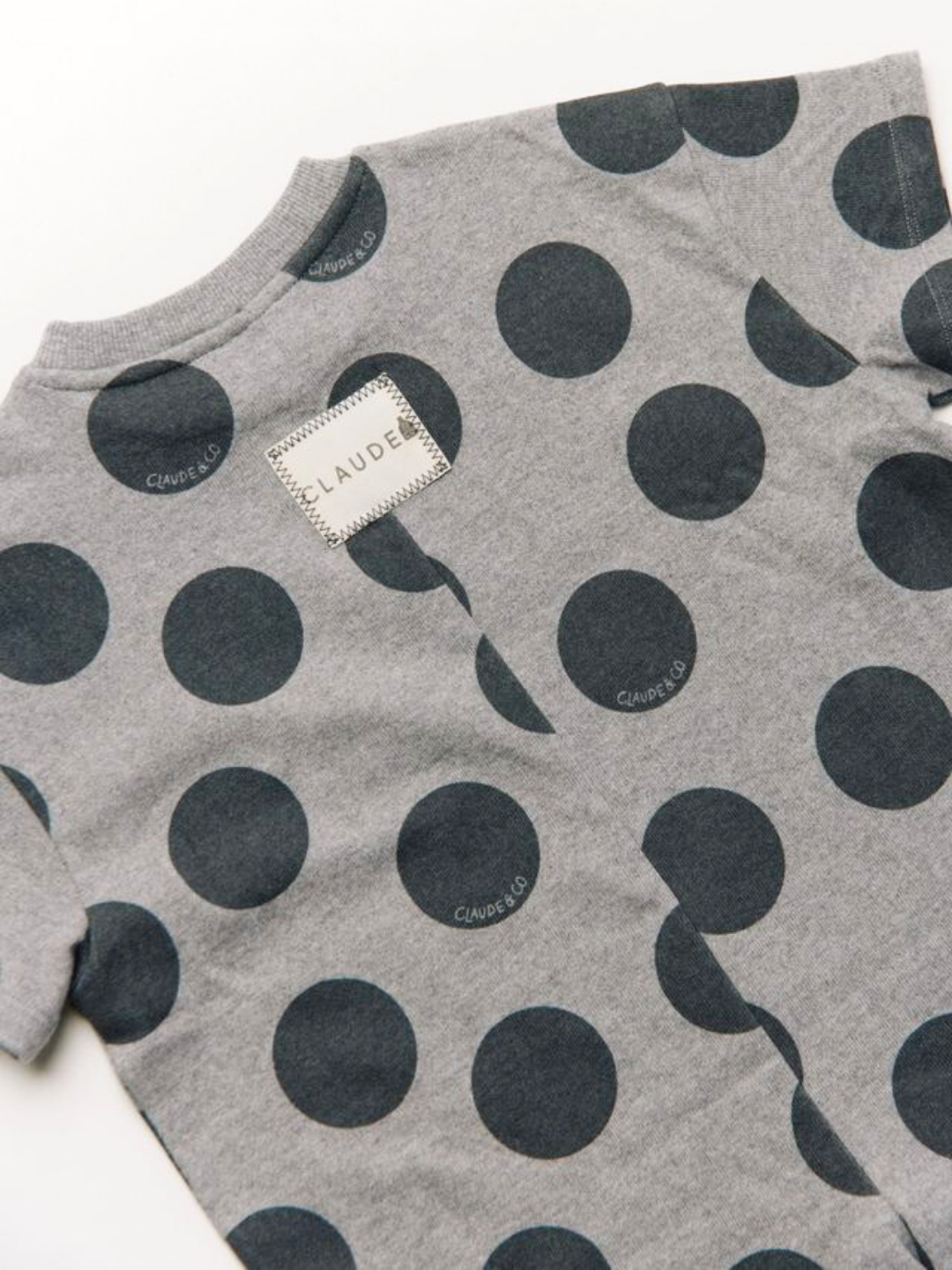 The OPAL MARL SPOT ROMPER is a gray short-sleeve outfit with large black polka dots and a white "CLAUDE" label sewn on the back near the neck.