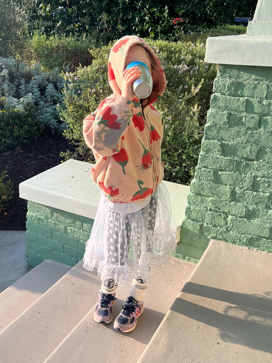 A child is wearing a tulle layer skirt that is see through over polka dot leggings, with a big printed hoodie , chunky socks and purple sneakers.