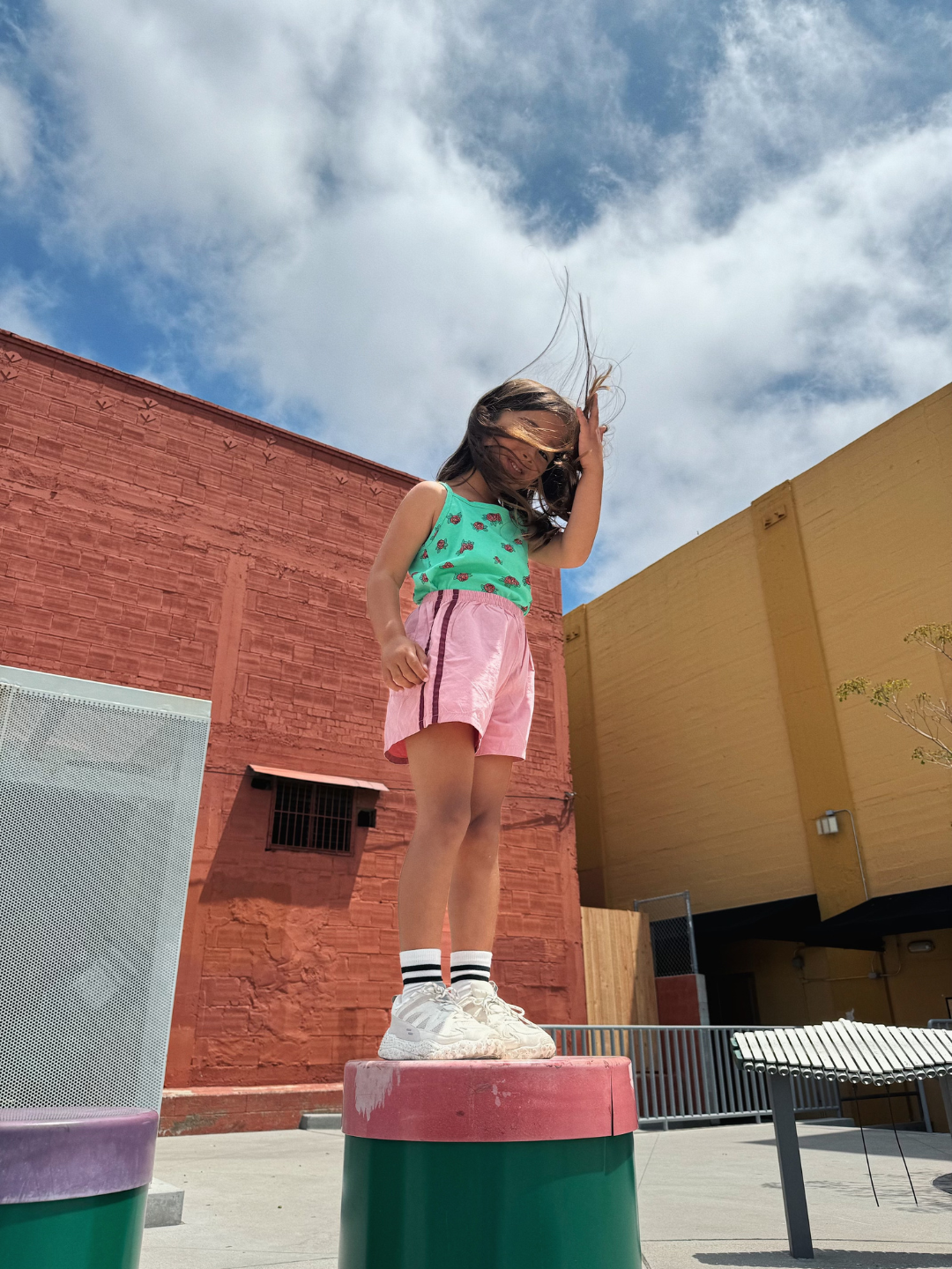 Green | Girl wearing the kids' roses tank top with pink shorts with maroon stripes down the side. She is standing outdoors in a courtyard, on a pink and green step.