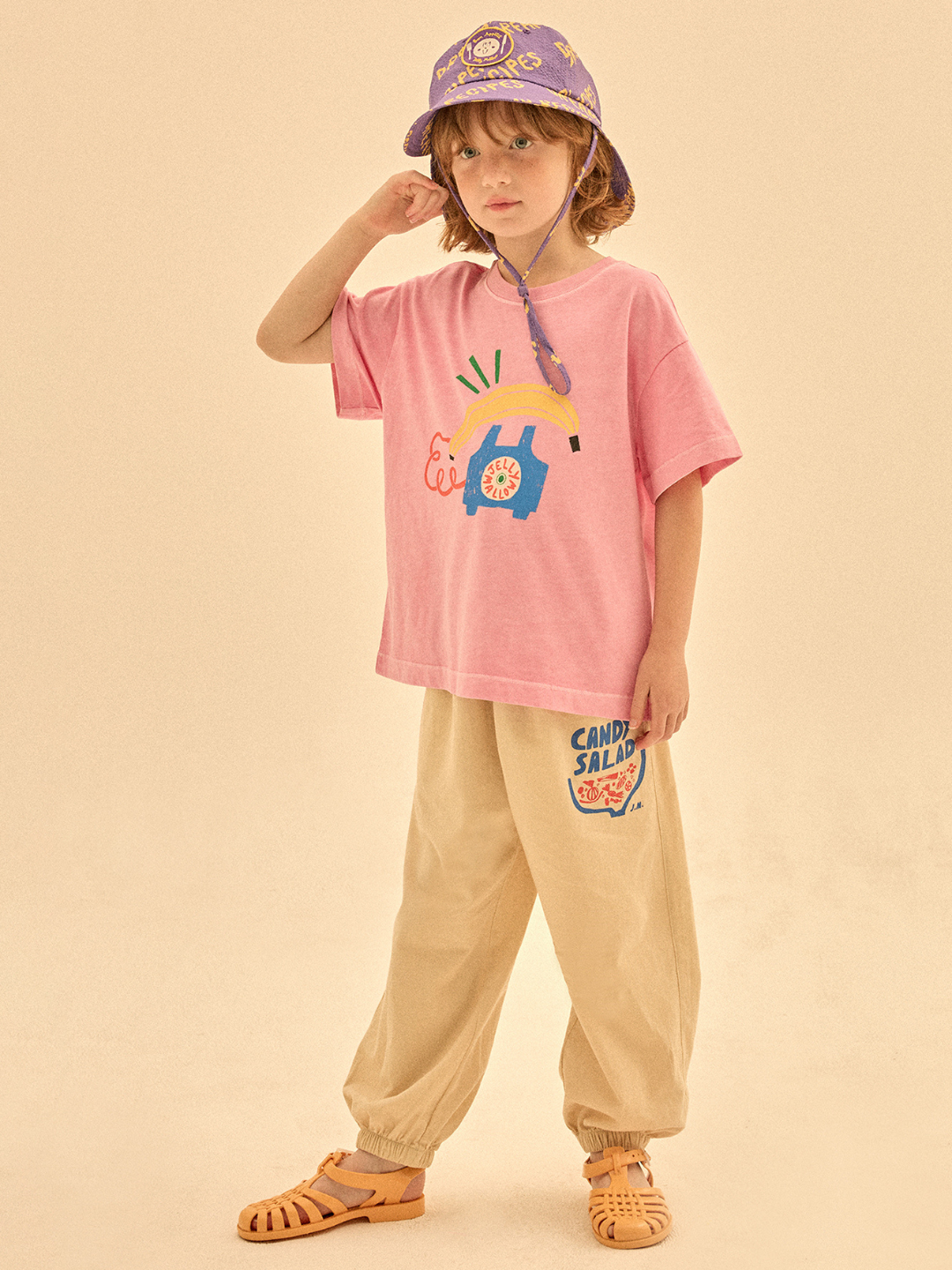 Child wearing a pink t-shirt with cartoon design and beige pants on a beige background