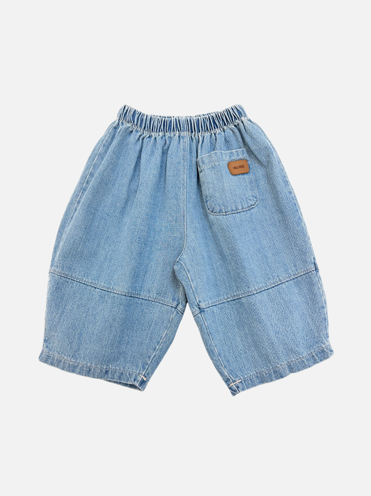 Image of Blue | The BABY BALLOON JEAN in blue features light denim, an elastic waistband, one back pocket with a small brown label, wide legs, and stitched detailing for extra style and comfort.