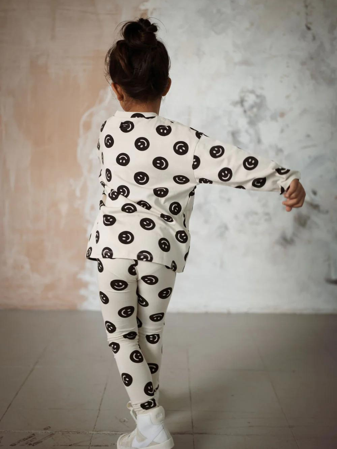 A back view of the cream colored, long sleeve shirt with a black smiley face pattern on a child.