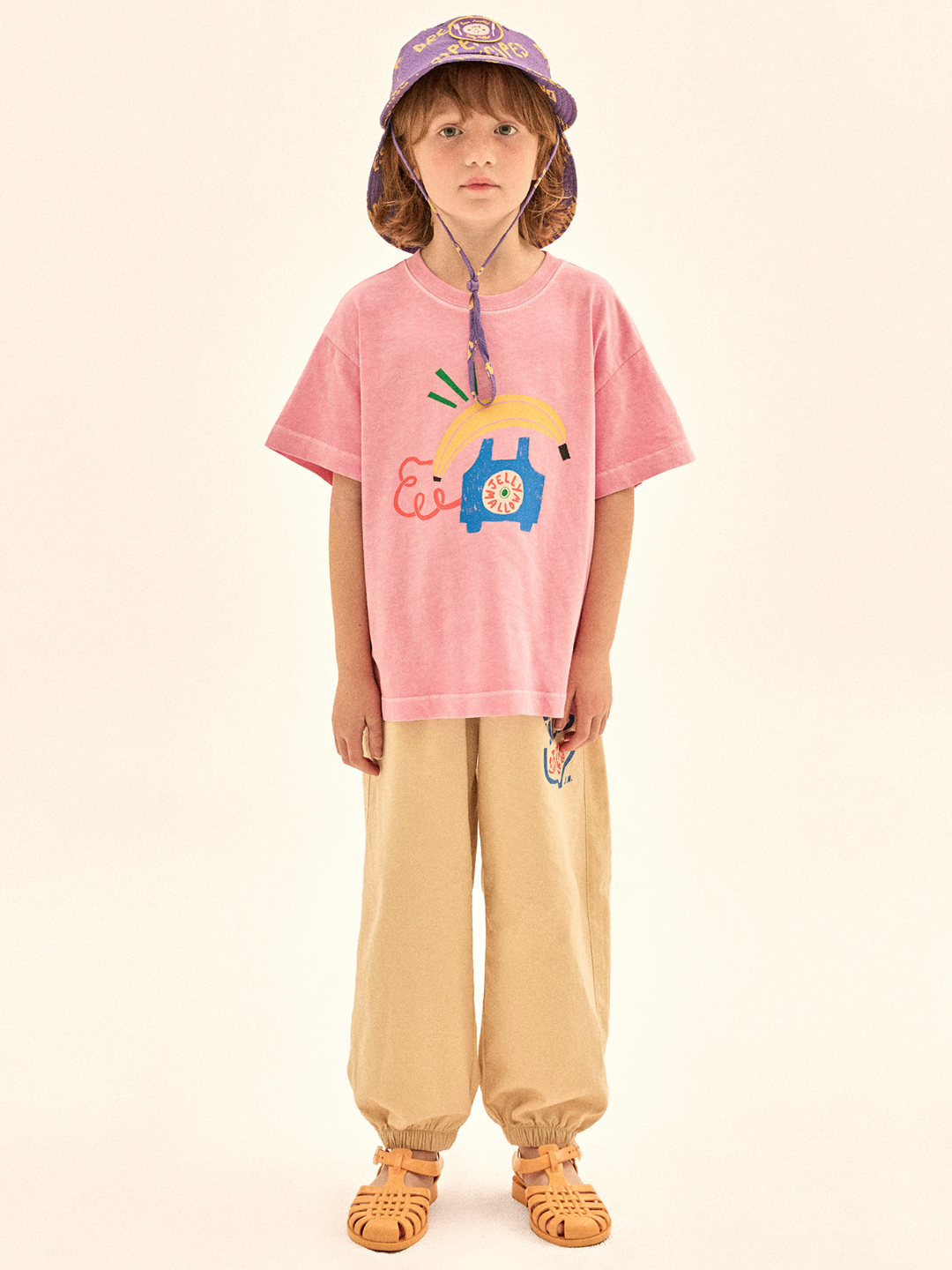 Child wearing a pink t-shirt with a colorful design and beige pants on a beige background