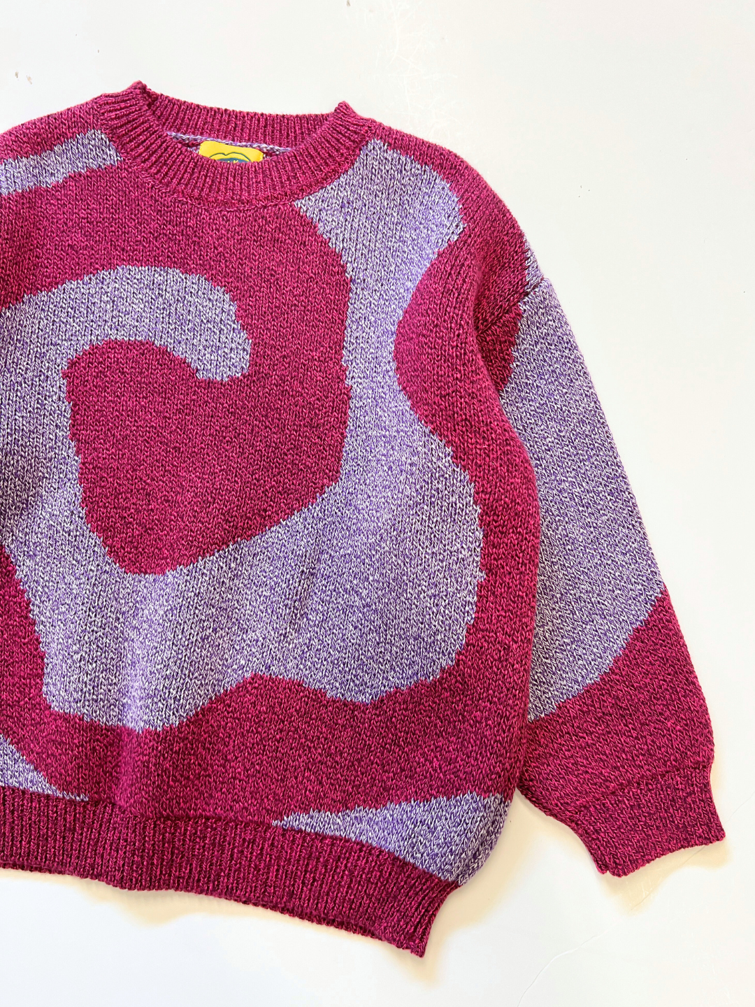Pink/Purple | The SWIRL SWEATER is a knit sweater with an abstract swirl design in burgundy and lavender, shown laid flat on a white surface.