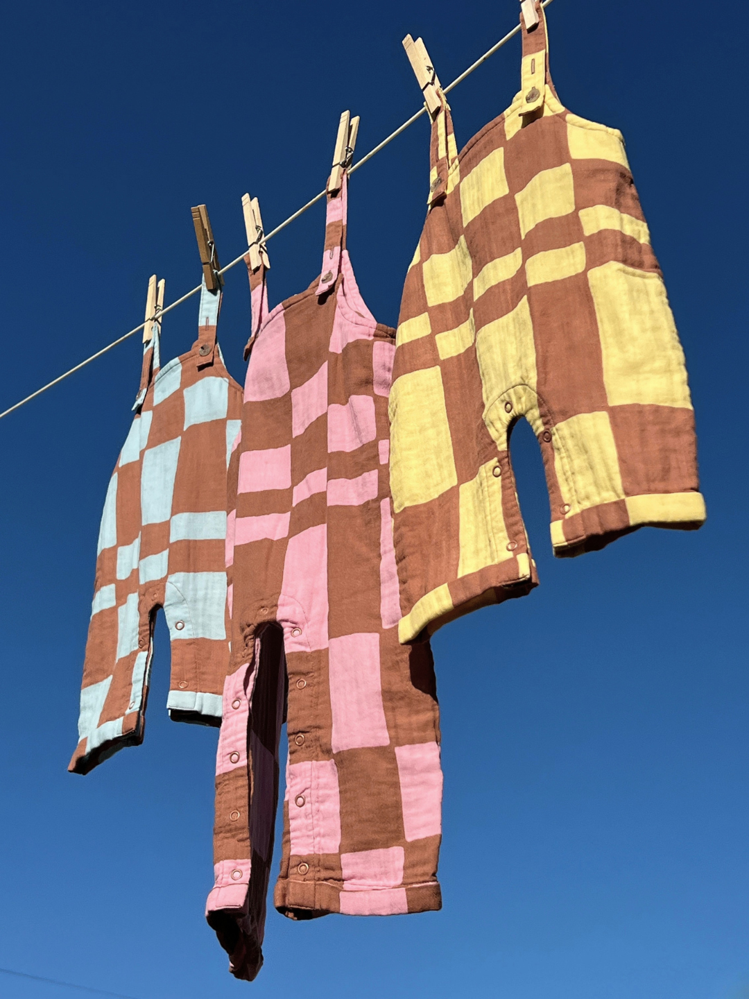 Pink Checkers | Colorful checkered rompers hanging on a clothesline against a clear blue sky.
