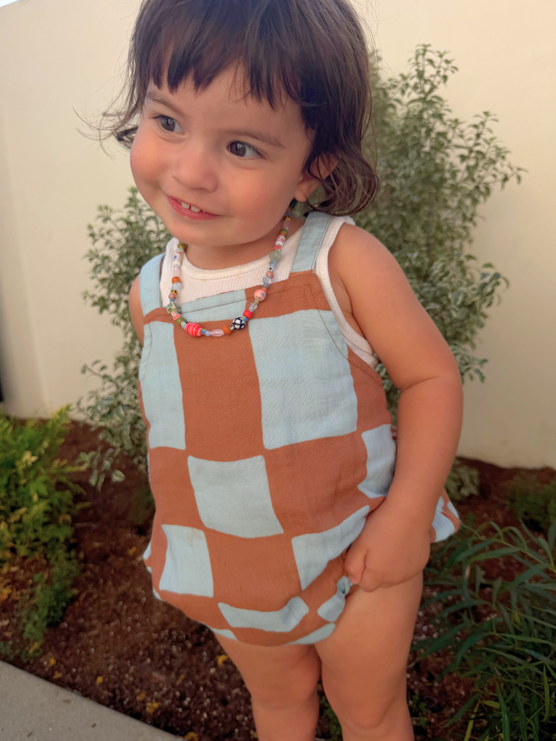 Blue Checkers | Child wearing a blue and brown checkered romper with plants in the background