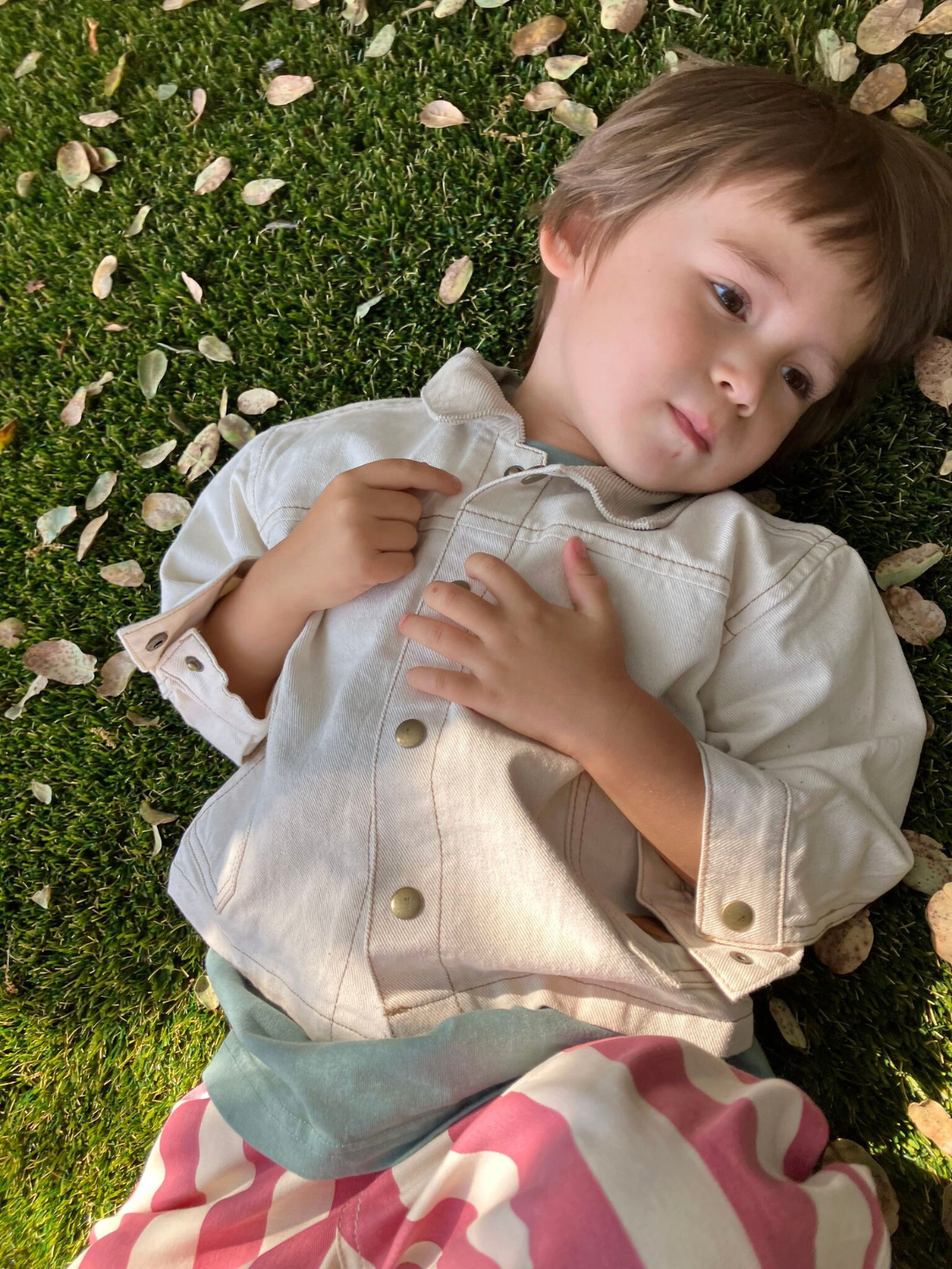 Natural | A kid laying on grass, wearing the Weekender Jacker in Natural.
