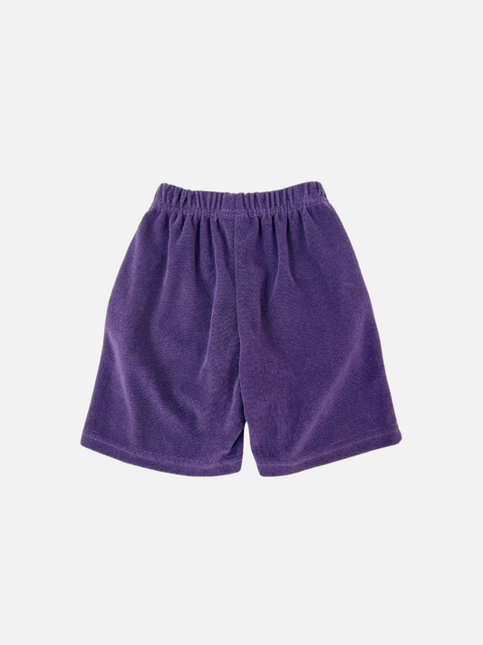 Second image of The TULIP TERRY SHORTS are purple cotton shorts featuring an elastic waistband and a flower graphic near the hem. They offer a slouchy fit, ideal for casual days. This fun and comfortable style is from a popular Korean kids' brand.