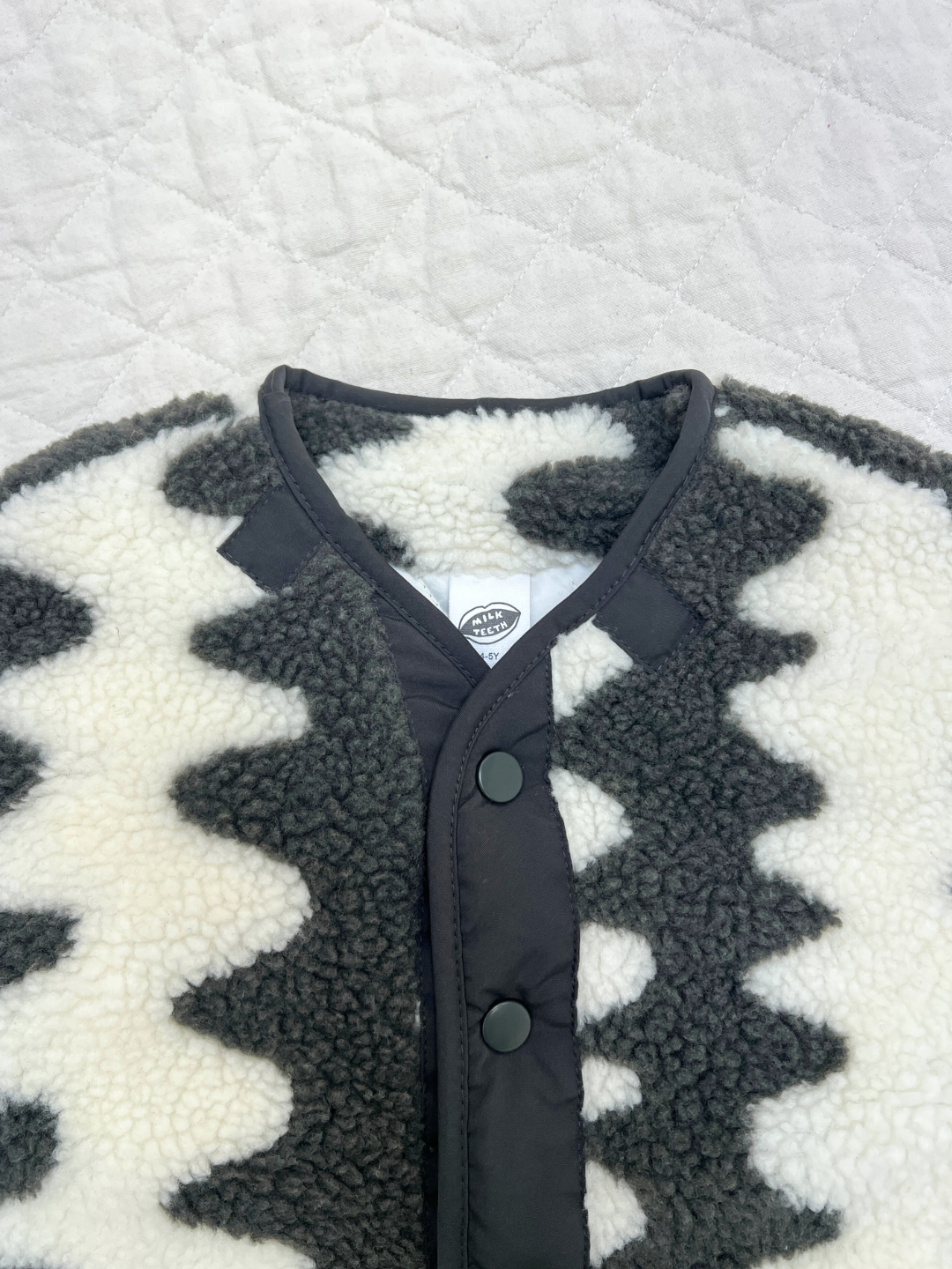 Charcoal | A close-up of the WAVELENGTH SHERPA JACKET—a black and white zigzag fleece winter jacket featuring black buttons, a visible collar, brand tag, and a cozy quilted interior.