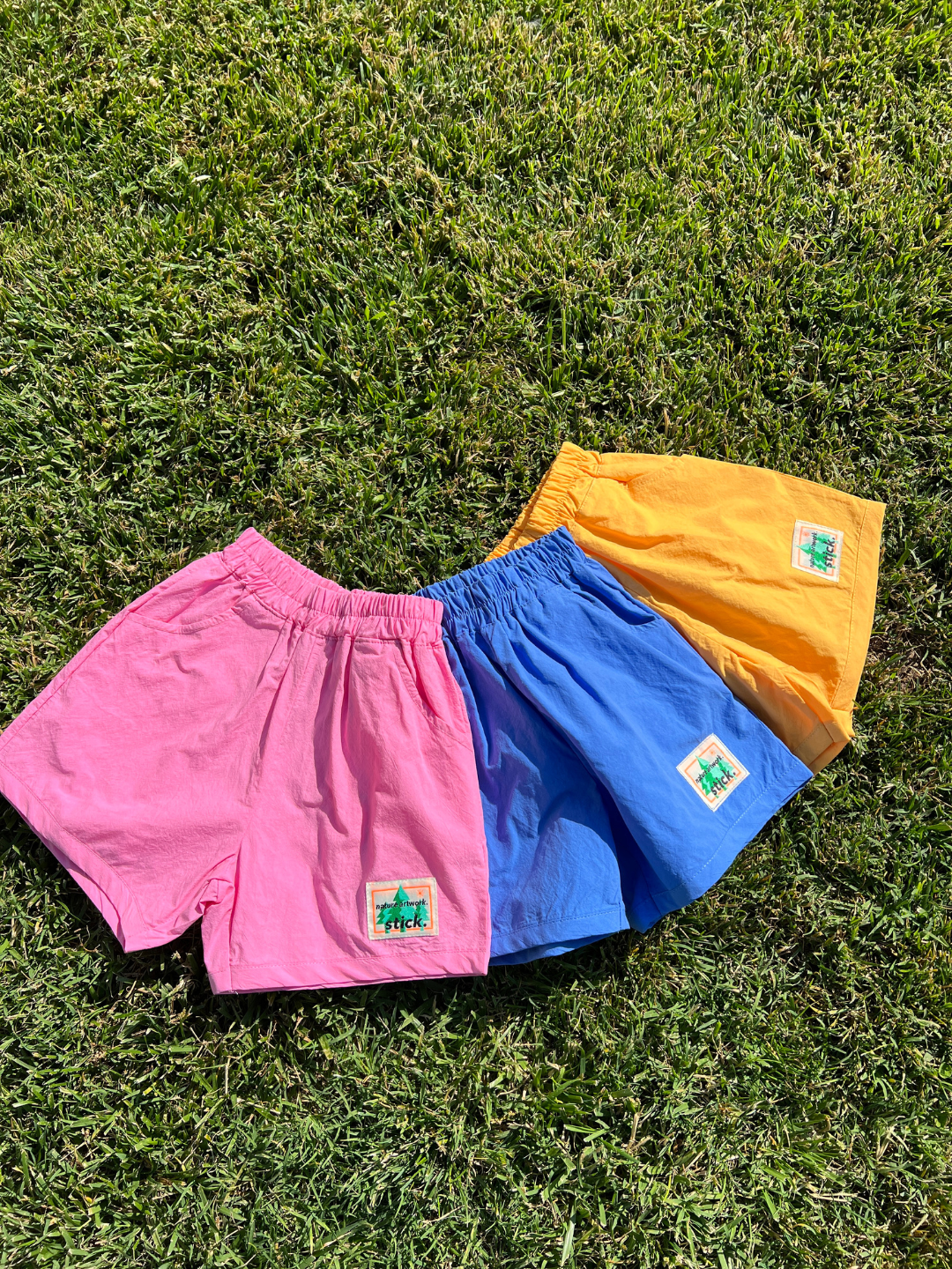 Pink, blue and orange kids' shorts arranged on grass.