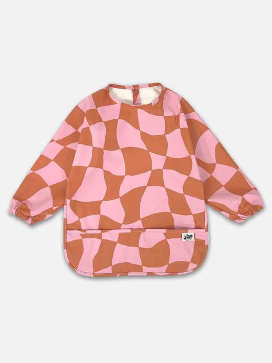 Image of Pink Checkers | A front view of the long sleeve light pink and rust wavy checked bib with a front pocket.
