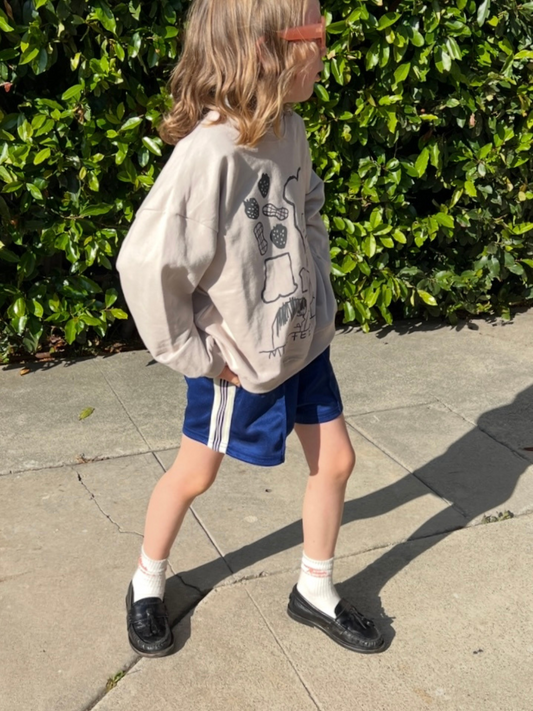 Second image of RETRO TRACK SHORTS: Blue kids’ shorts with white side stripes, elastic waistband, and a small white logo on the left leg. Classic vintage-inspired design displayed on a plain white background.