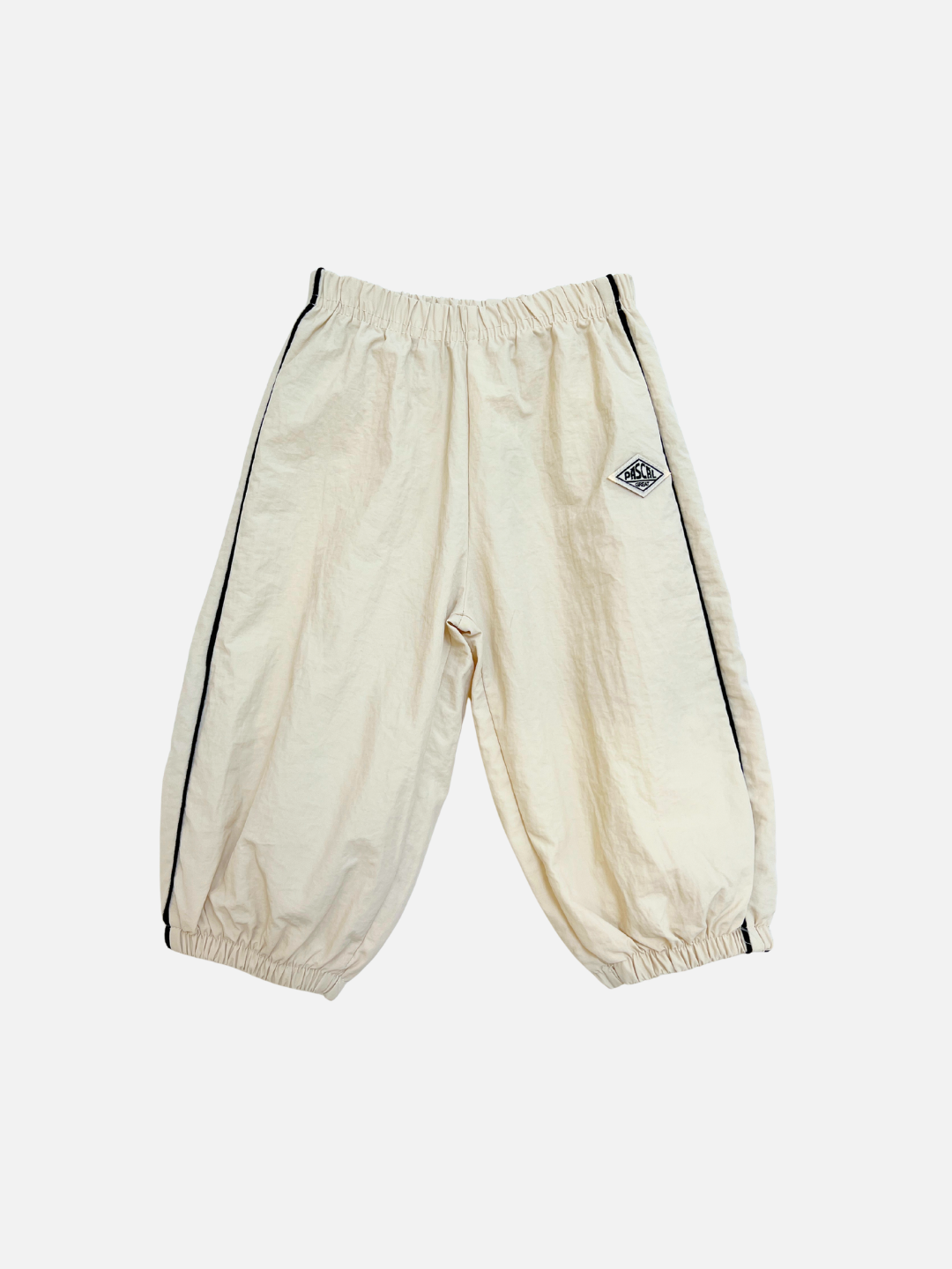 MINI WARMUP PANTS in stone feature a baggy fit, elastic waistband and cuffs, black side piping, and a small diamond-shaped logo patch on the left leg.