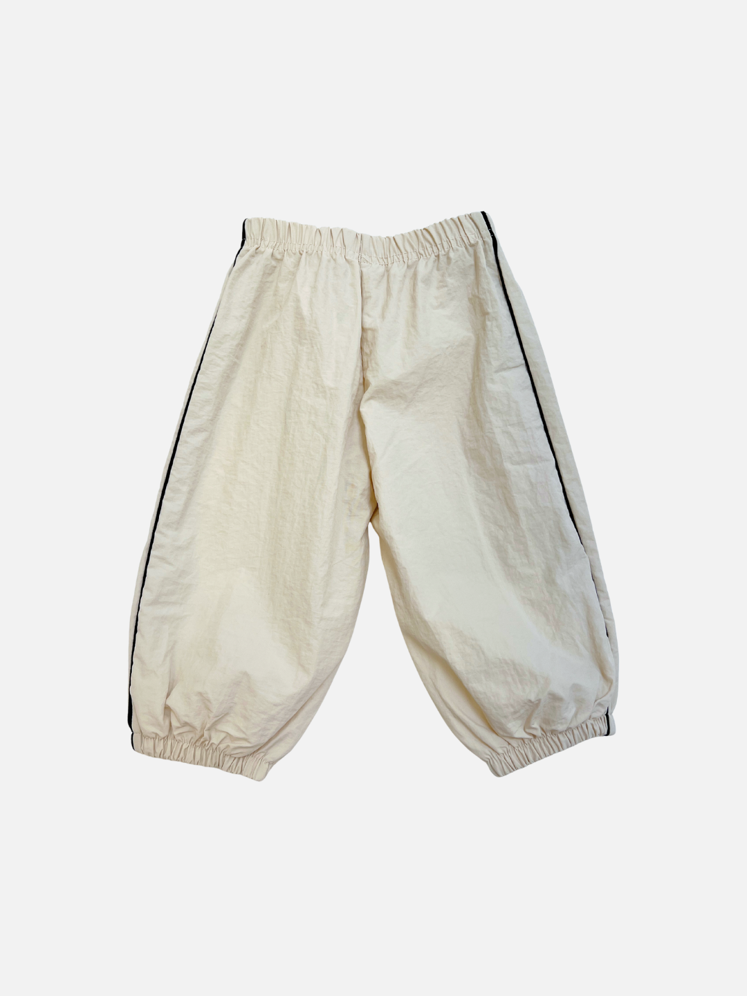 Stone | The MINI WARMUP PANTS are loose-fitting, off-white pants with an elastic waistband and cuffs, accented by a sleek black stripe down the sides.