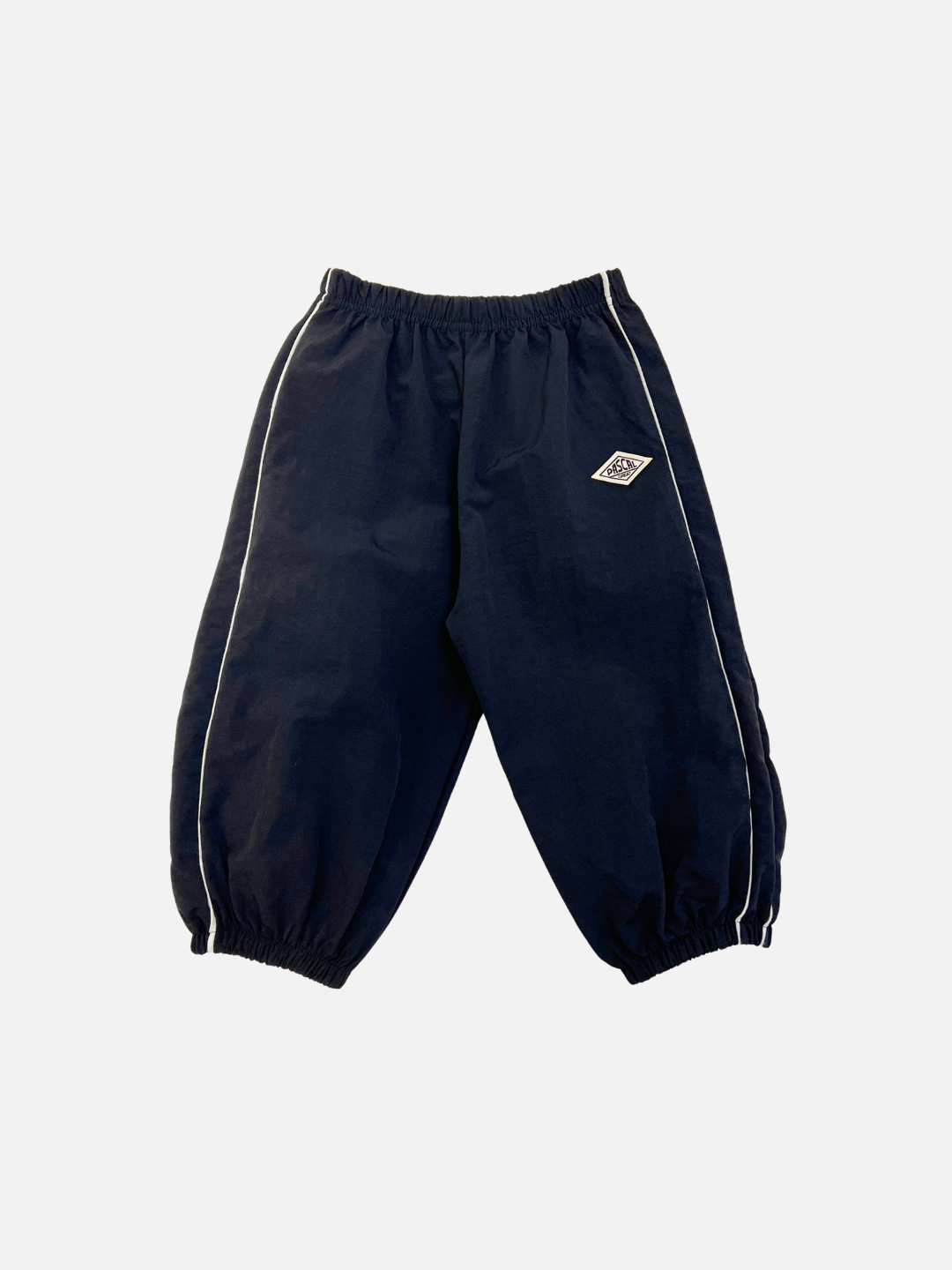 The MINI WARMUP PANTS are black with white side piping, an elastic waistband and cuffs, and a small white geometric logo on the upper left leg.