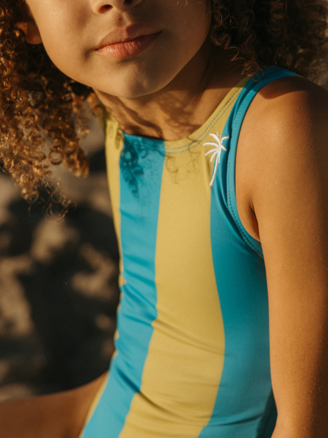 A child is wearing a Retro Stripe Swimsuit in Kelp