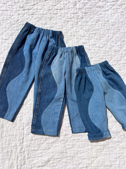 Image of Three pairs of the kid's up cycled wave jeans are laid flat on the quilt, all are one-of-a-kind made from second hand denim. 