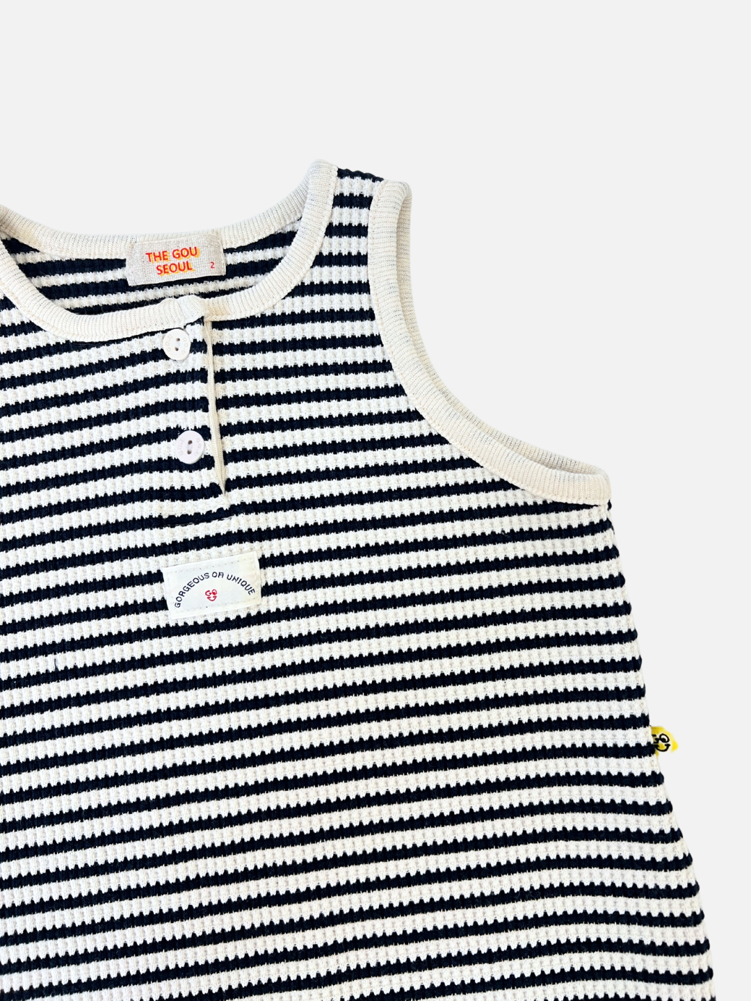 Navy | The STRIPE WAFFLE ROMPER SET is a sleeveless knitted top with black and white stripes, featuring three buttons by the collar and a text patch on the chest, made from textured waffle cotton. Perfectly matches a bonnet set or baby jumpsuit for a coordinated look.