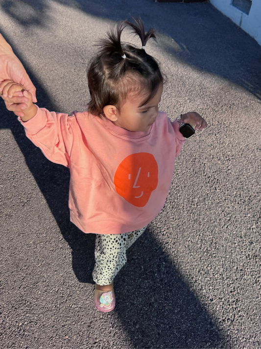 Second image of A pink BOXY POTATO SWEATSHIRT by OXOX CLUB, made from organic cotton, features a simple orange face graphic on the front and is displayed laid flat on a white background.