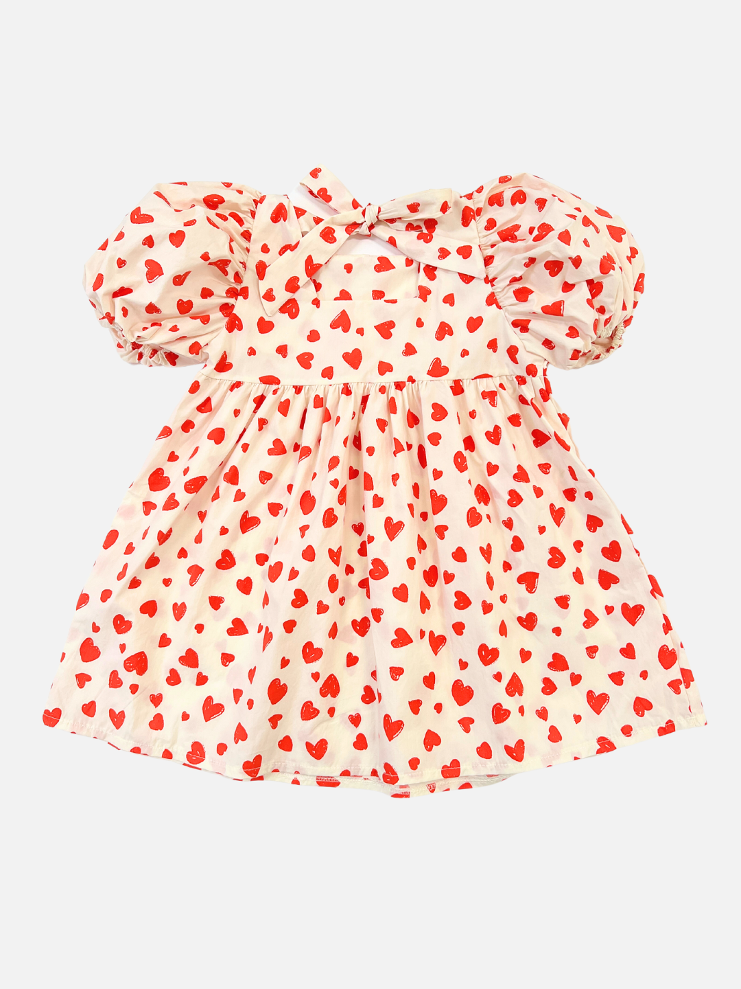 A kids' puff-sleeved dress with red hearts on a white background, and bow tied at the neck, back view