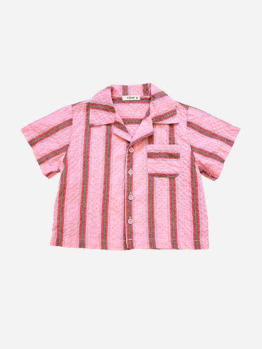 Image of The HAVANA STRIPE SHIRT is a vintage-inspired, short-sleeved pink cotton shirt with vertical red, black, and white stripes and a single chest pocket, shown laid flat against a white background.