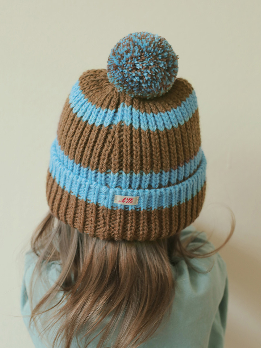 Blue | A child is wearing the blue pompom hat. 