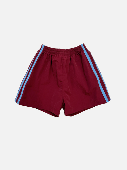 Image of Maroon | SPRINTER SHORTS in maroon, crafted from performance fabric with an elasticated waist and blue vertical side stripes, shown on a plain white background.