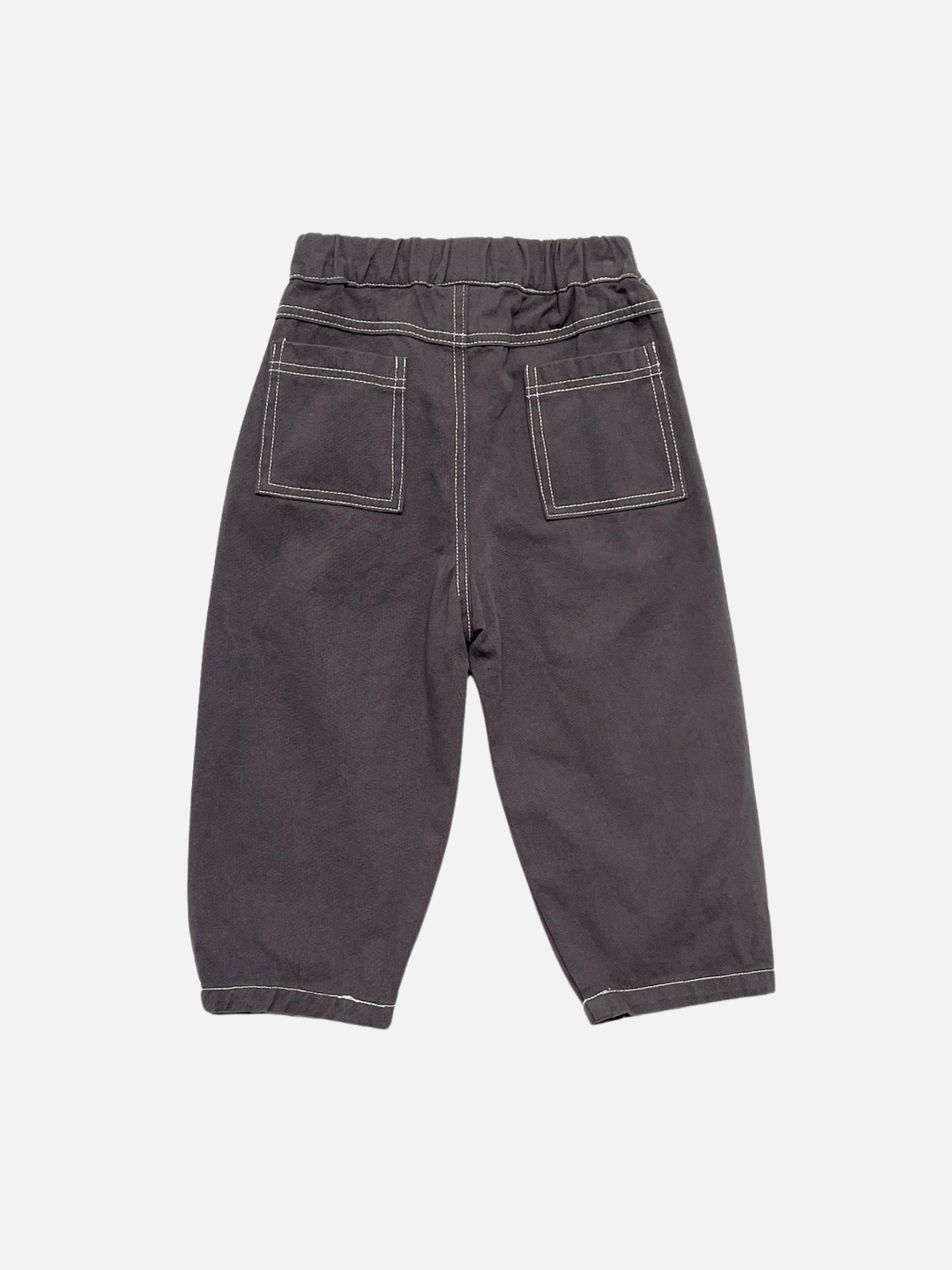 Charcoal | Back view of kids baggy dark grey pants with contrast white topstitching on back patch pockets, shown flat on a light grey background.