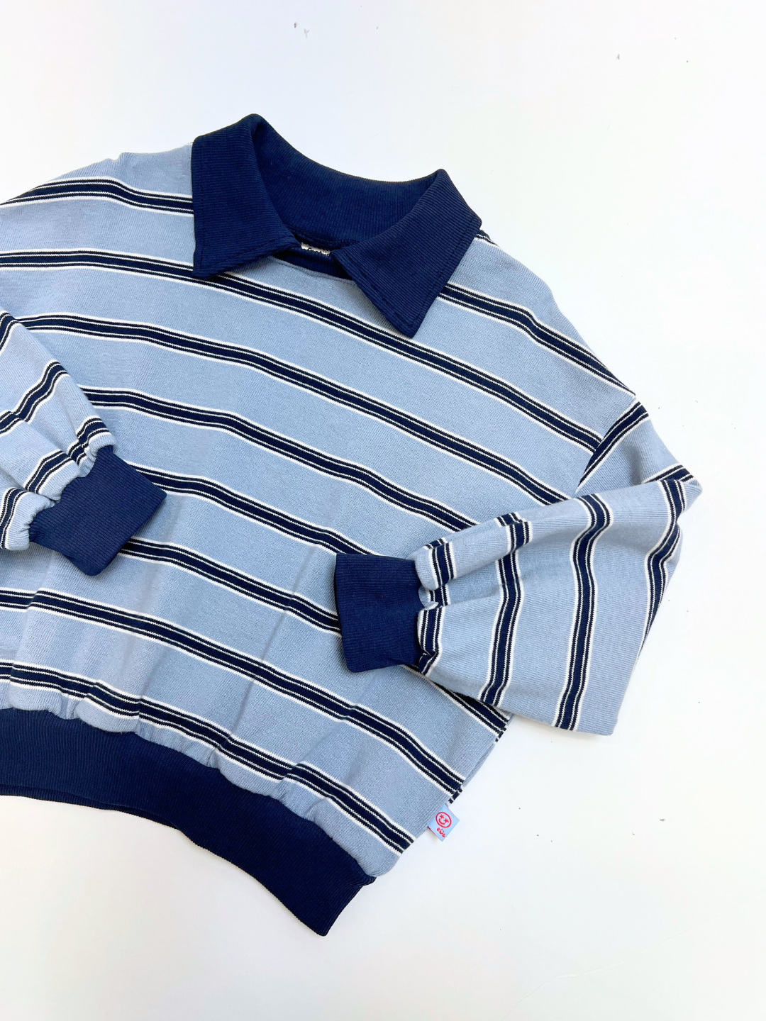 The GARY COLLAR SWEATSHIRT is a light blue, long-sleeve top with navy collar, cuffs, and hem, featuring stylish horizontal white and navy stripes, laid flat on a white surface.