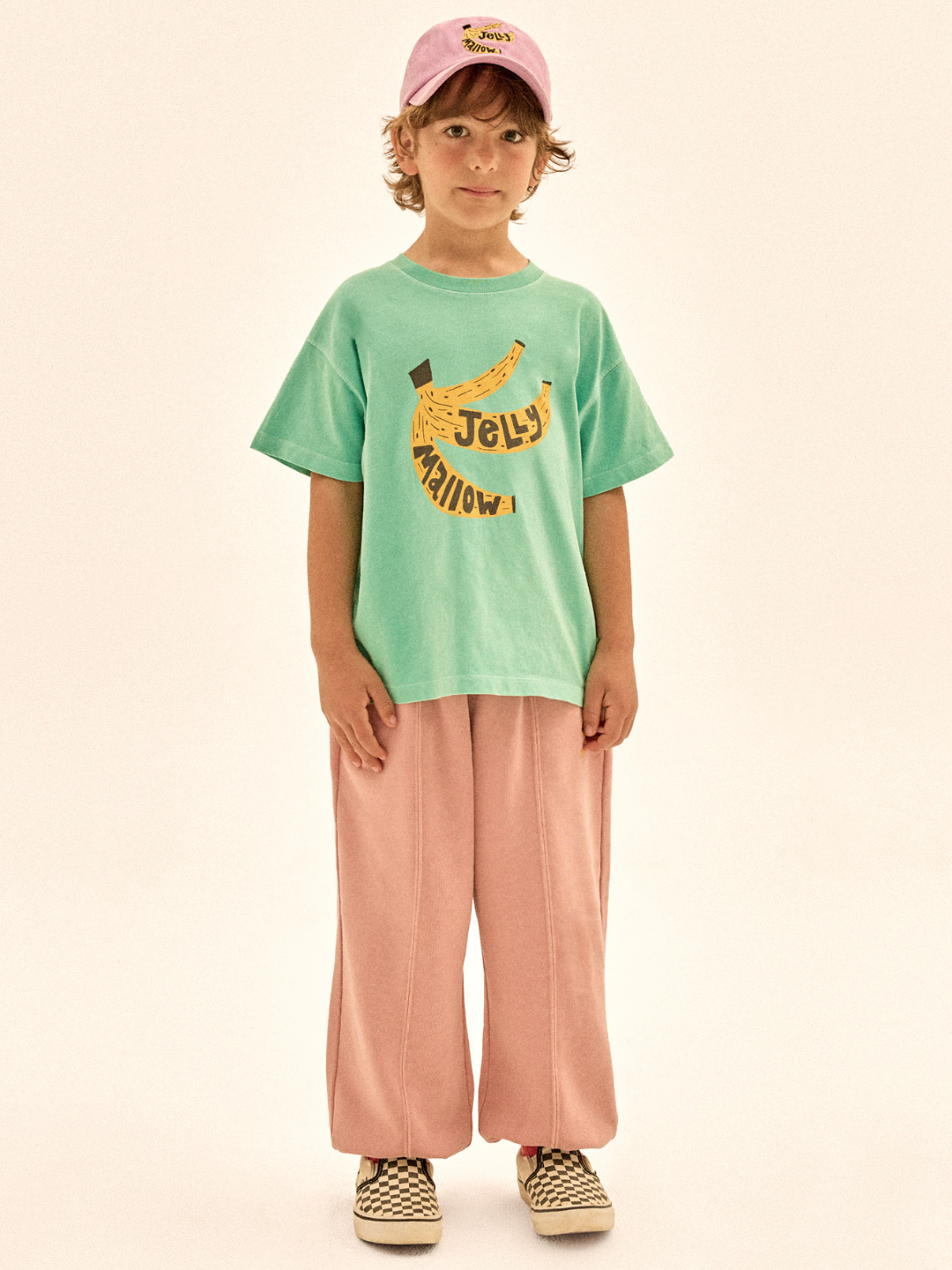 Child wearing a green t-shirt with text and pink pants on a beige background
