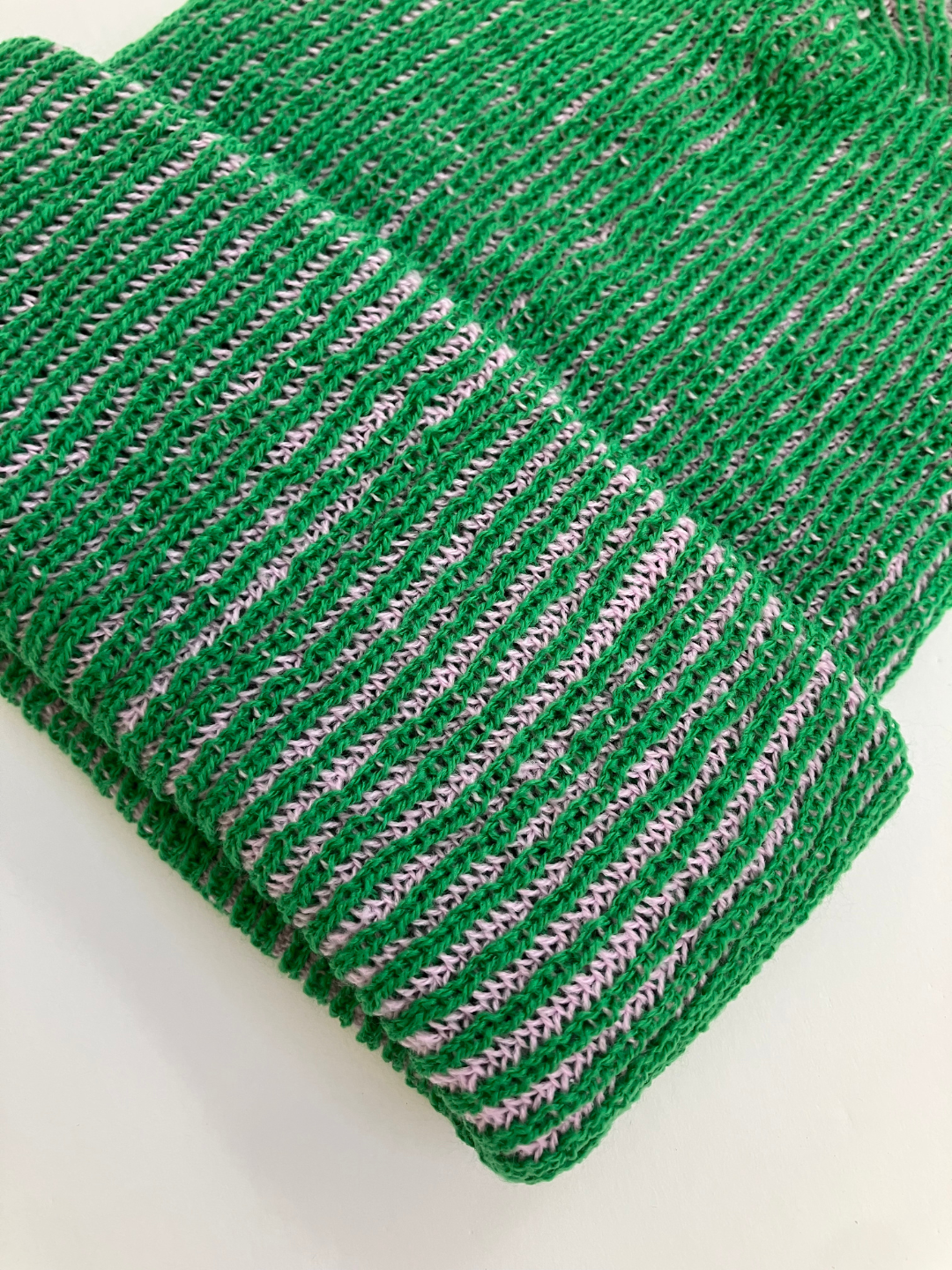 Front view of a kelly green ribbed beanie for big kids and adults, with a ribbed cuff. The ribbed texture reveals a second yarn color that's light purple.