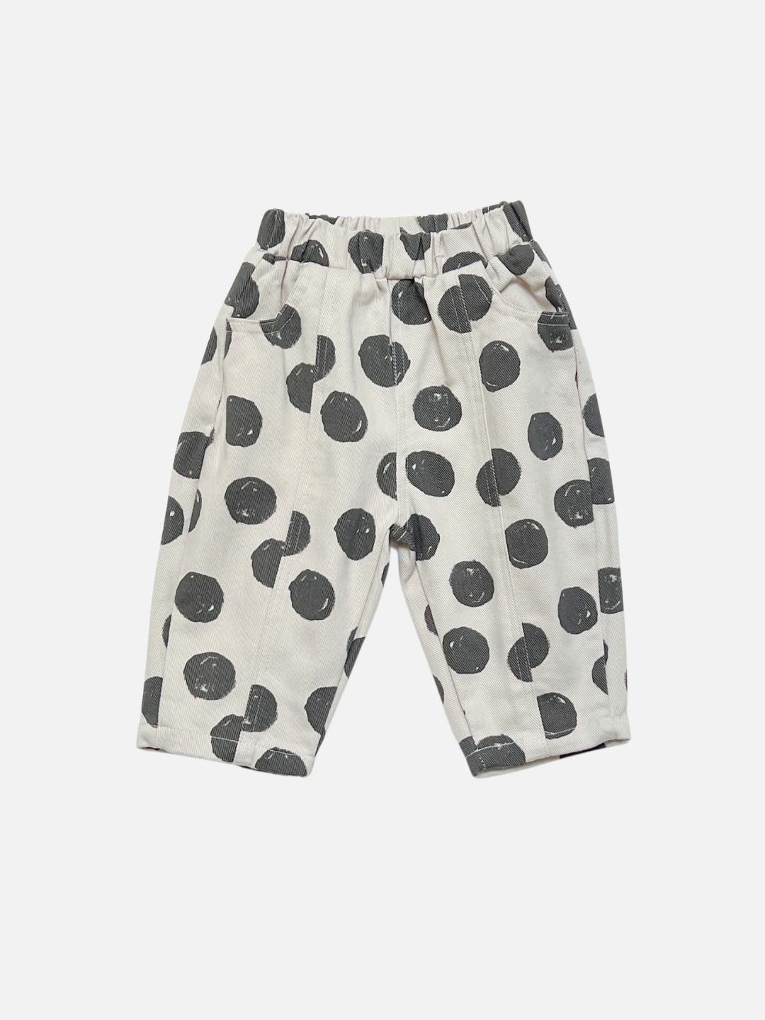 A pair of toddler's cream-colored pants with a black polka dot pattern, featuring an elastic waistband and side pockets, shown against a light gray background.