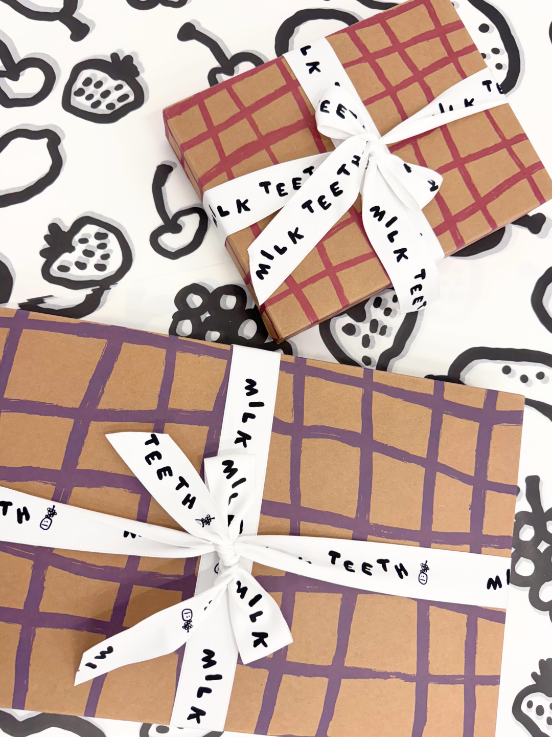 Gift Boxes with plaid brushstrokes wrapping and 'Milk Teeth' ribbon on a patterned background