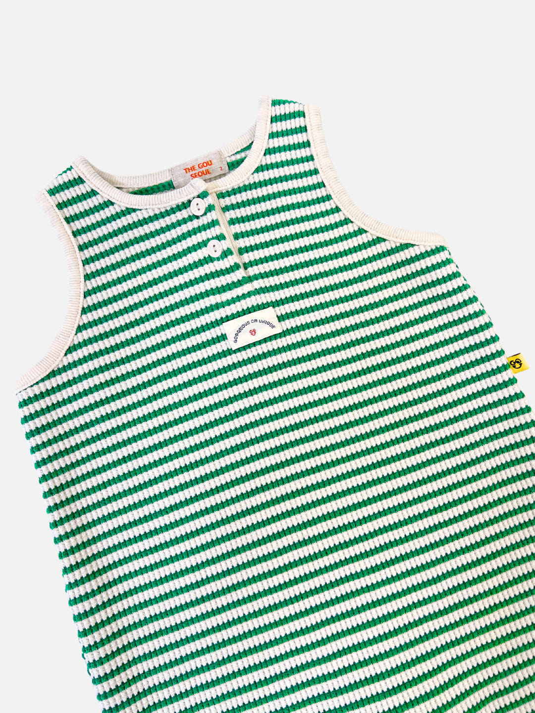 Green | The STRIPE WAFFLE ROMPER SET is an adorable toddler shirt featuring a cheerful green and white striped pattern crafted from soft waffle cotton, buttons on the upper part, and a small pocket with a smiley face design, perfectly complementing any bonnet set for a charming look.