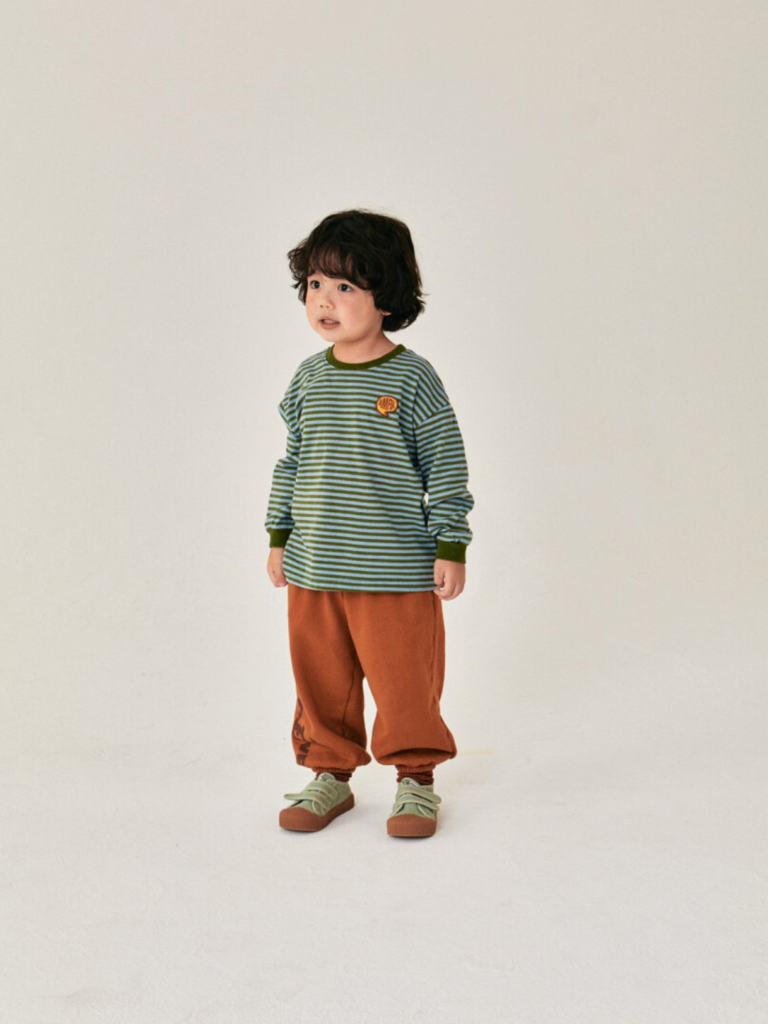 Child is wearing Comma Striped Longsleeve in Sky/Olive with orange baggy pants