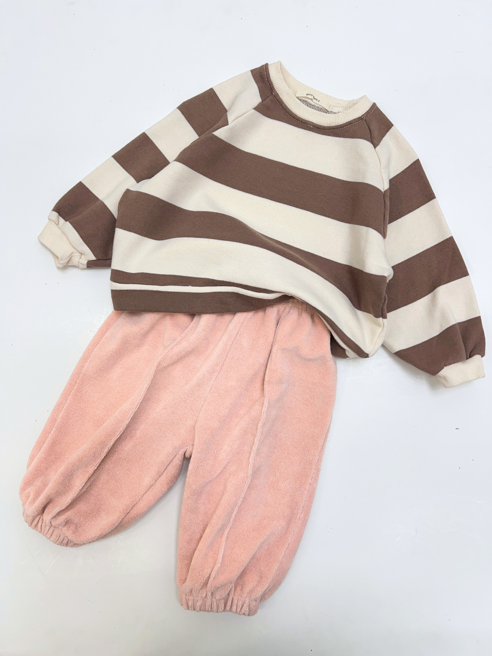 The STRIPE BABY SWEATSHIRT, a brown and white striped cotton terry long-sleeve top from a Korean baby brand, is paired with loose-fitting light pink pants, both displayed flat on a white background.