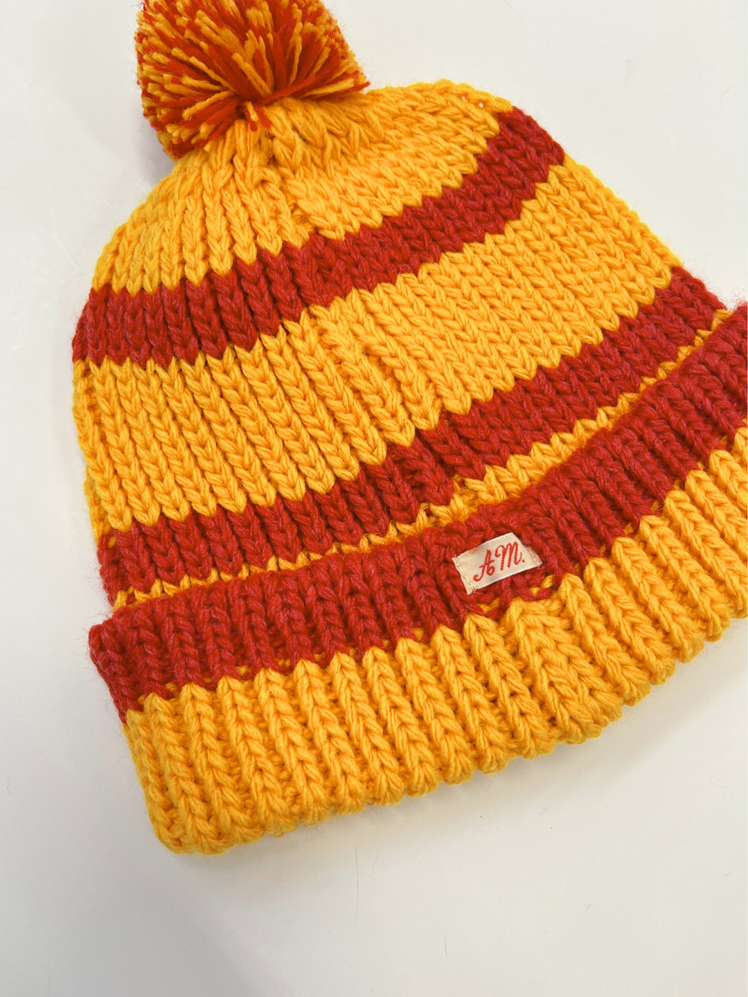 Yellow | Yellow pompom hat is laid flat on white background. 