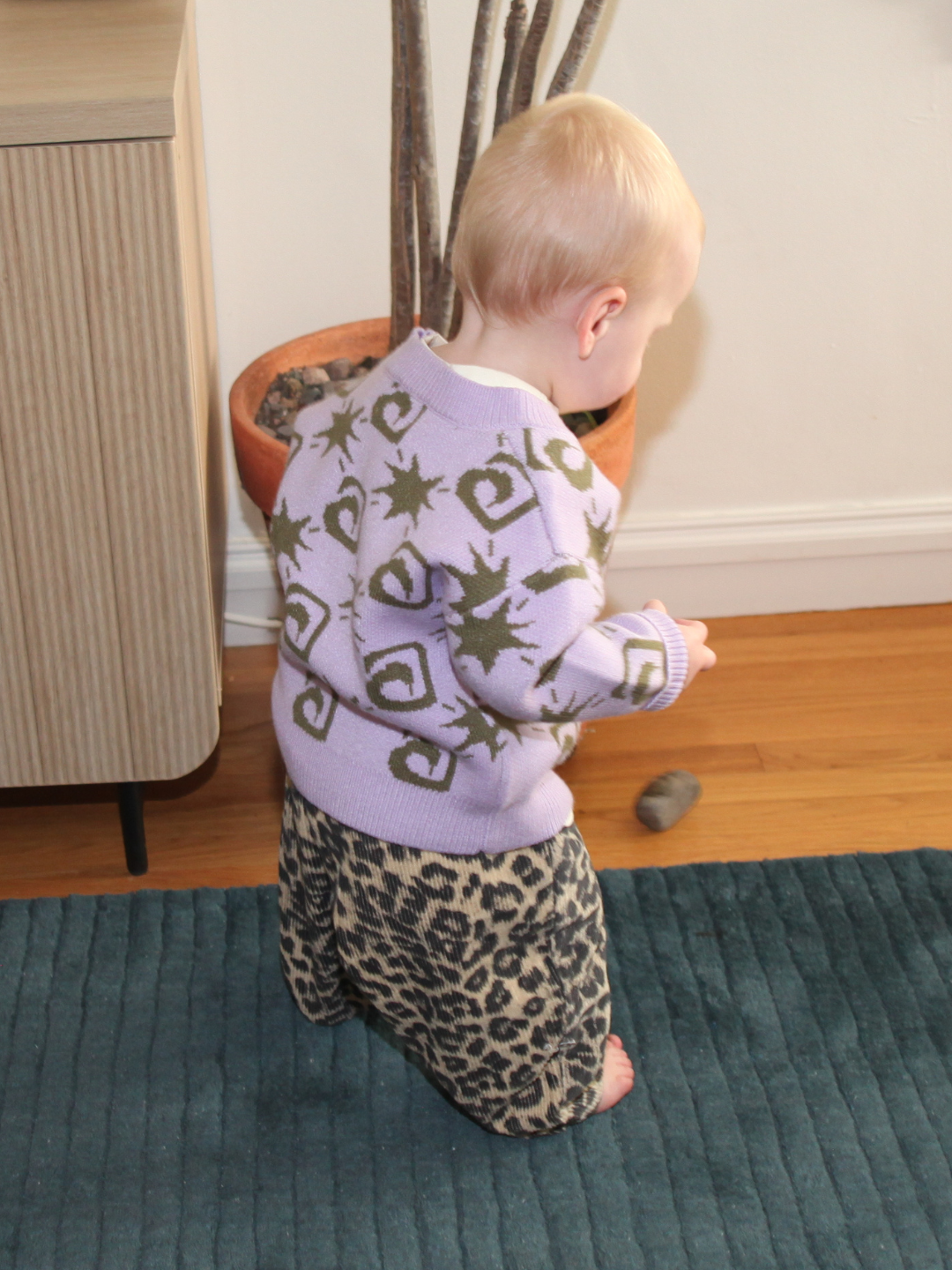 Child wearing a patterned sweater and leopard print pants on a blue rug.