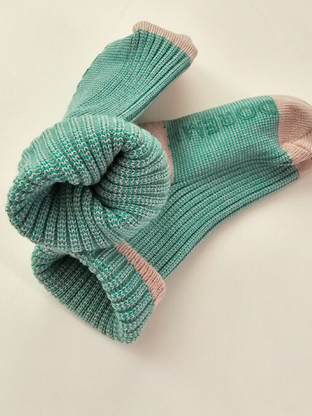 Two green wool socks with gray toes and heels placed on a white surface, one laid flat and the other rolled. These colorful ribbed socks from the TRIO SOCK SET by the Korean brand Doremi add a playful touch to any outfit.