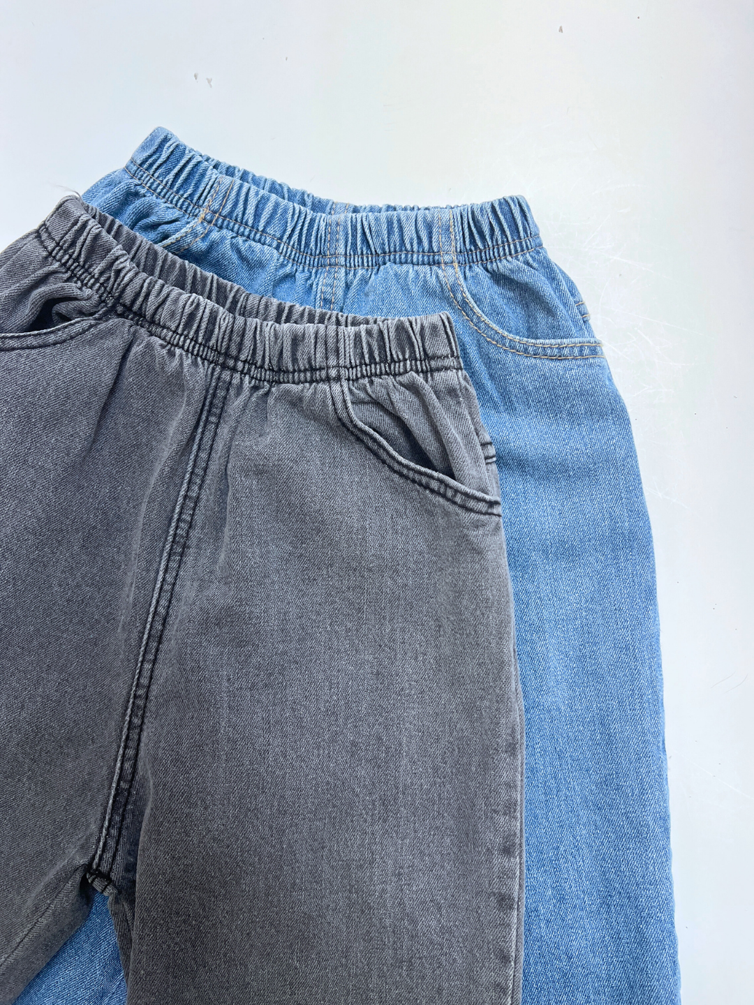 Two pairs of PEPPER JEAN elastic-waist jeans, in grey and light blue, are laid flat and overlapping on a white surface—ideal for everyday comfort.