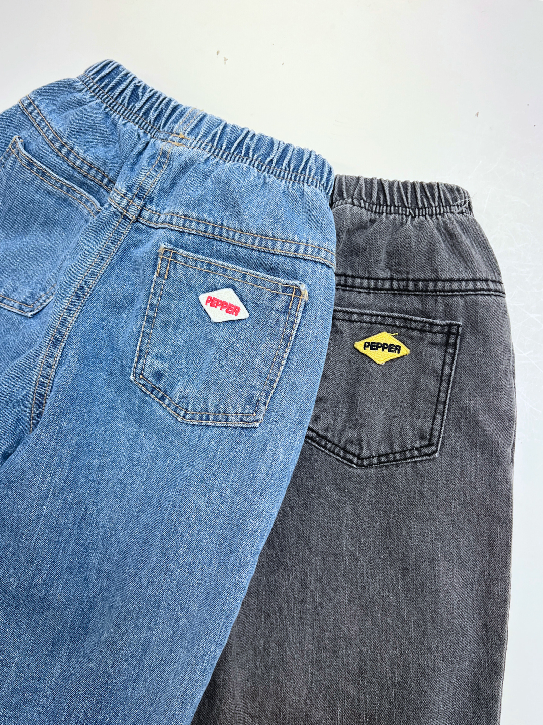 Grey | Two pairs of PEPPER JEAN elastic waist jeans—one blue, one black—each with a back pocket label reading "PEPPER" in a unique color.