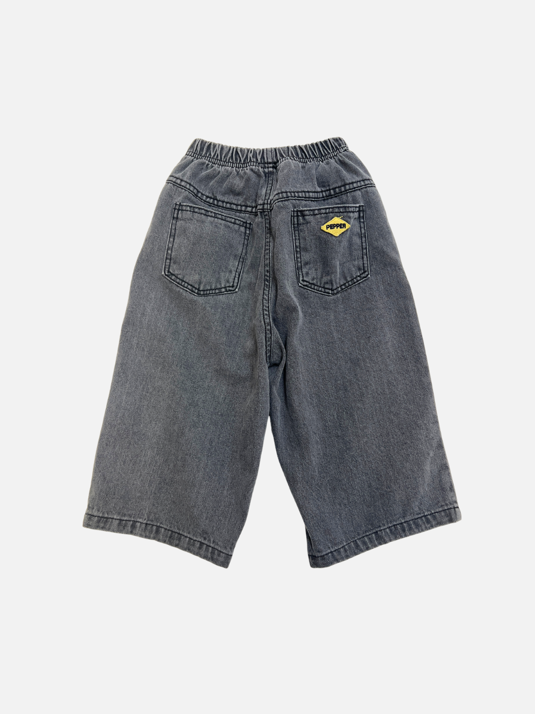 Grey | PEPPER JEAN: Loose-fitting gray denim shorts with two back pockets, one adorned with a small yellow patch featuring embroidered text.