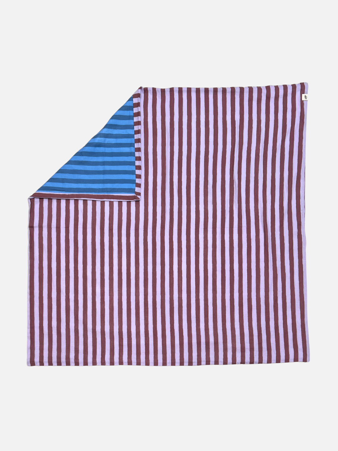 The organic cotton reversible quilt has maroon and purple stripes, and is is shown flat on a light grey background, with a corner folded back revealing its blue striped underside.