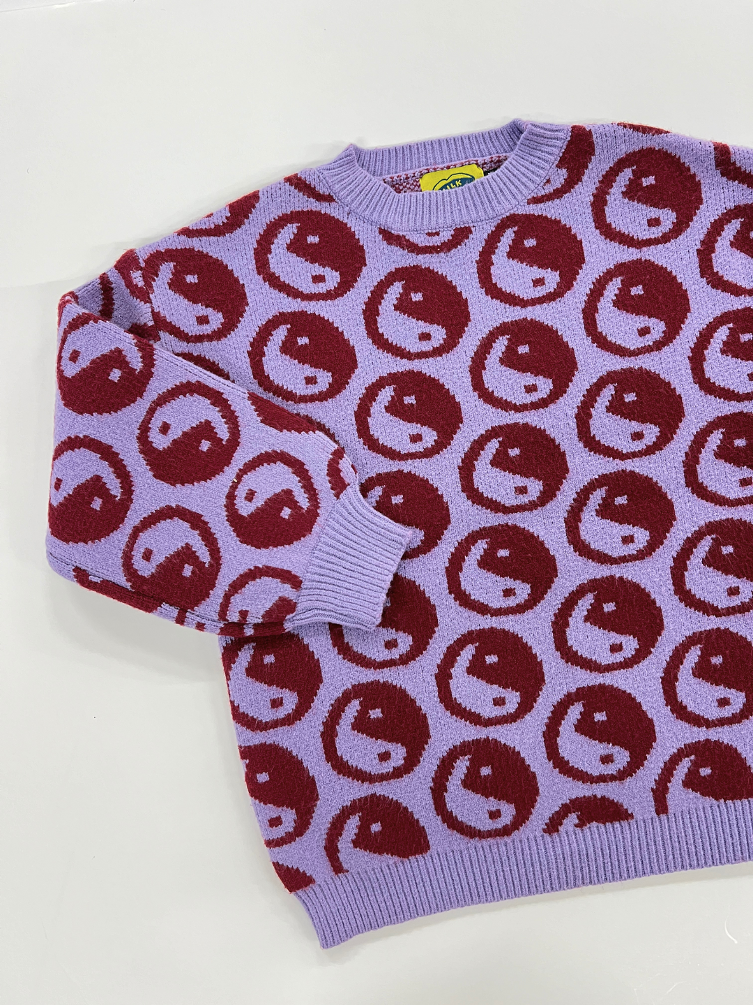 The COSMOS SWEATER, a super-soft purple crewneck adorned with a pattern of yin yangs, is laid flat on a white surface.