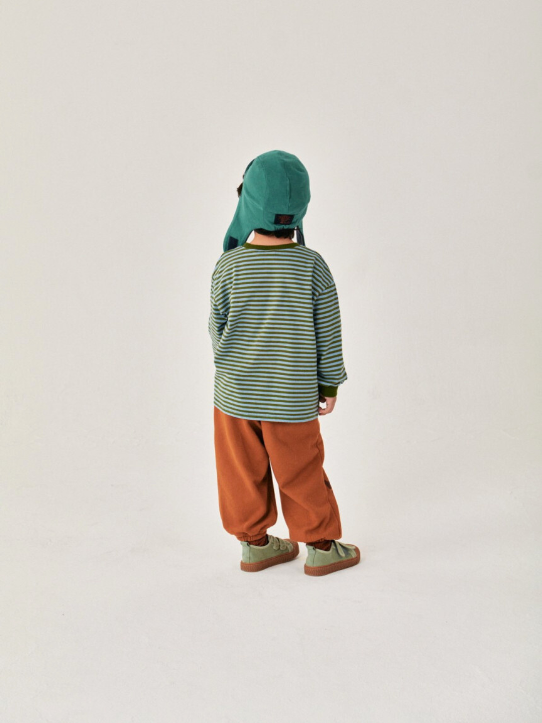 Child is wearing Comma Striped Longsleeve in Sky/Olive with baggy orange pants back view 