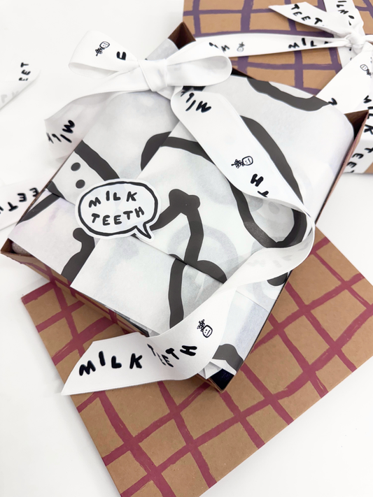 Second image of Gift Boxes with plaid brushstrokes wrapping and 'Milk Teeth' ribbon on a patterned background