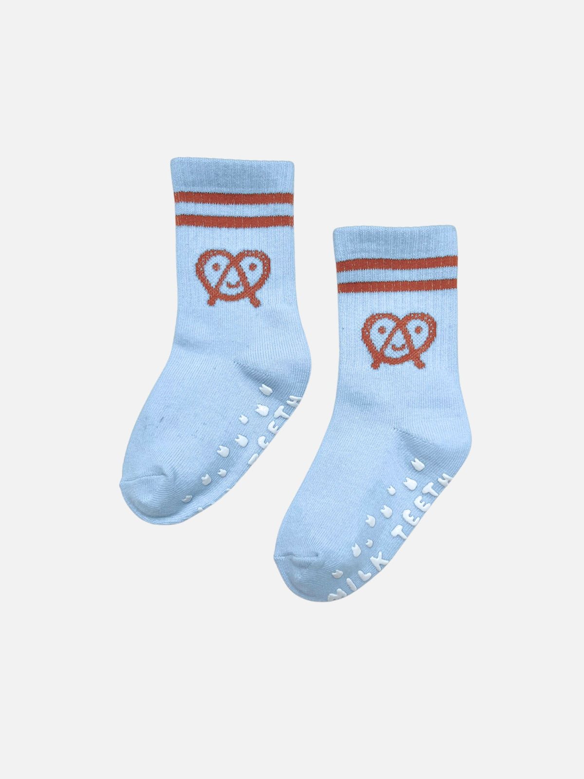 RIBBED GRIP SOCK in light blue with two brown stripes at the cuff, a brown pretzel icon, and white anti-skid grips on the soles reading “MILK TEETH”.