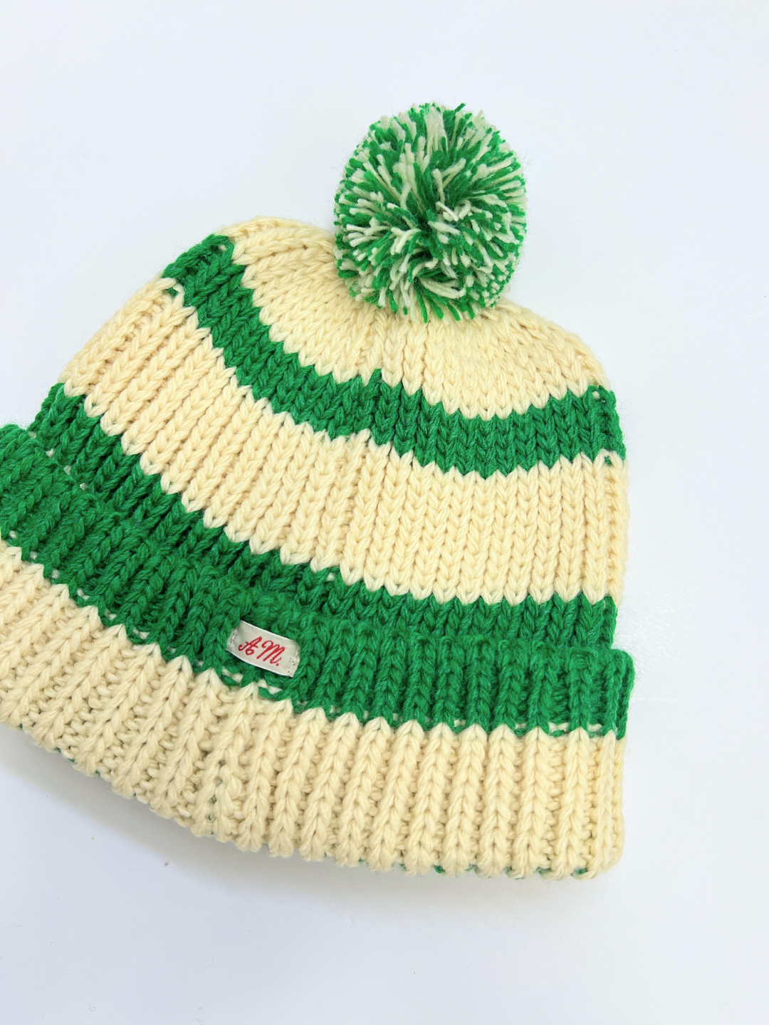 Green | The green pompom hat is laid flat on white background