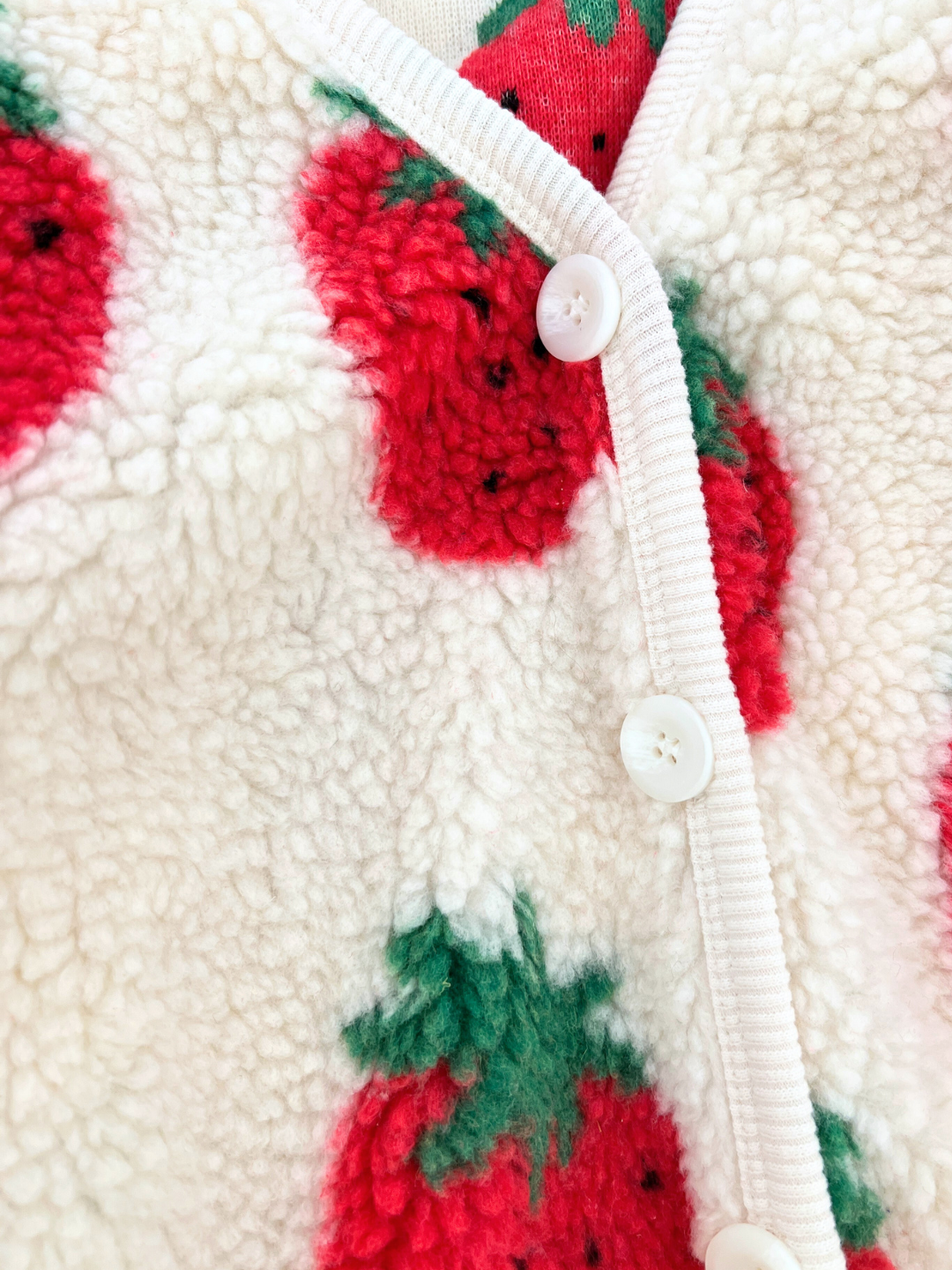 Close-up of a fluffy white STRAWBERRY SHERPA JACKET, designed by the Korean kids brand Hanab, featuring a charming strawberry print with white buttons down the front.